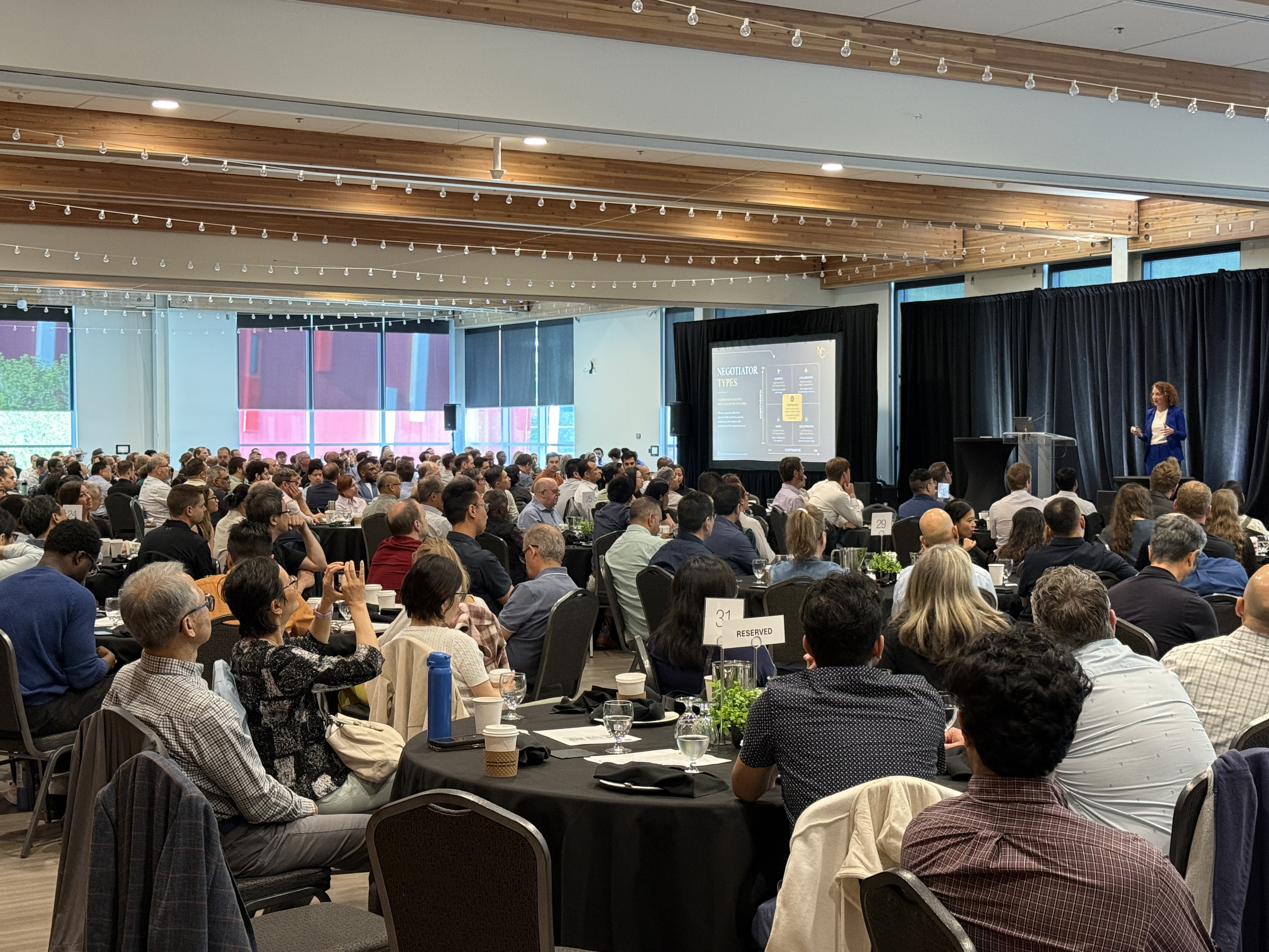 A Negotiations Collective speaker leading a keynote in a full conference room